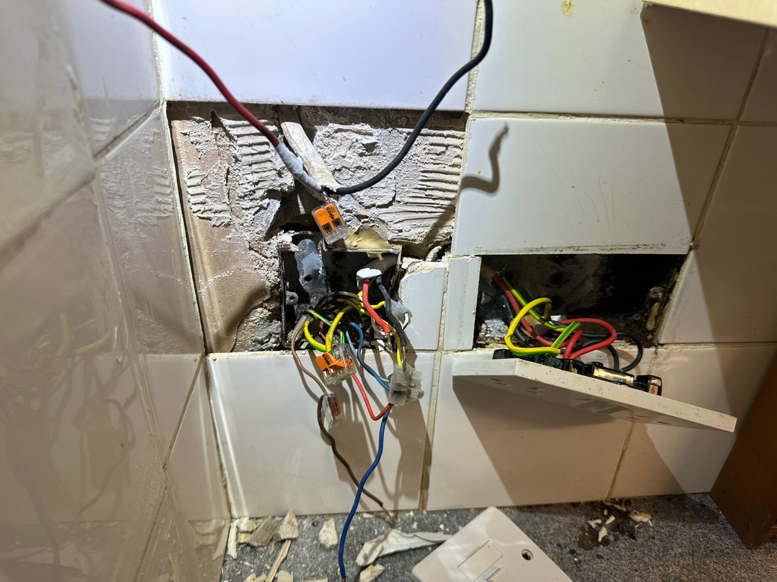 Exposed socket back-boxes and wiring on a tiled kitchen wall